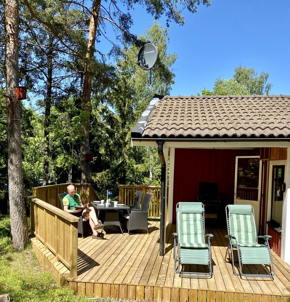 A wooden deck with outdoor furniture, a satellite dish, and a red building with a tiled roof.