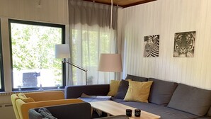 Un salon moderne avec un canapé gris, des fauteuils jaunes, une table basse en bois et une grande fenêtre avec des rideaux.
