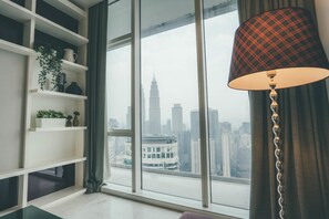 A modern room with a large window, a view of a city skyline, and a lamp with a plaid lampshade.