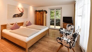 Quarto com cama de madeira, almofadas xadrez, uma cadeira com estampa de vaca, televisão e porta que dá para uma varanda.