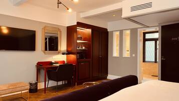 Una habitación de hotel moderna con una cama, un escritorio con una silla, un televisor, un armario y un baño visible a través de una puerta abierta.