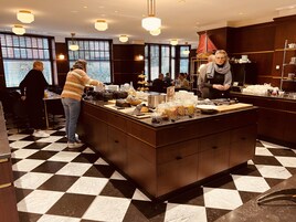 A checkered floor, a buffet counter with food items, and people in a dining area.