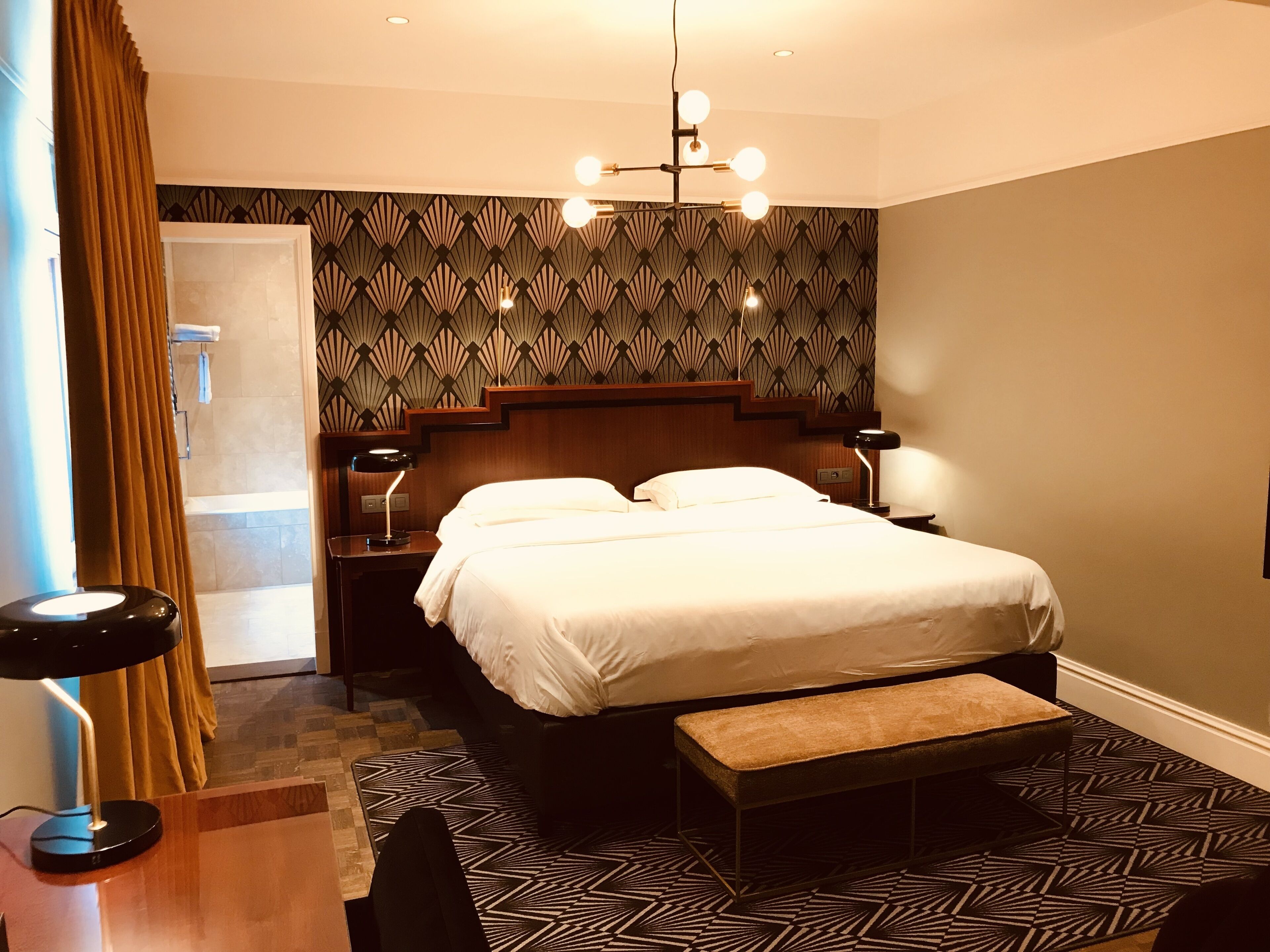 Een hotelkamer met een bed, bedlampen, een bankje, een bureau en een kamerbreed tapijt met dessin.