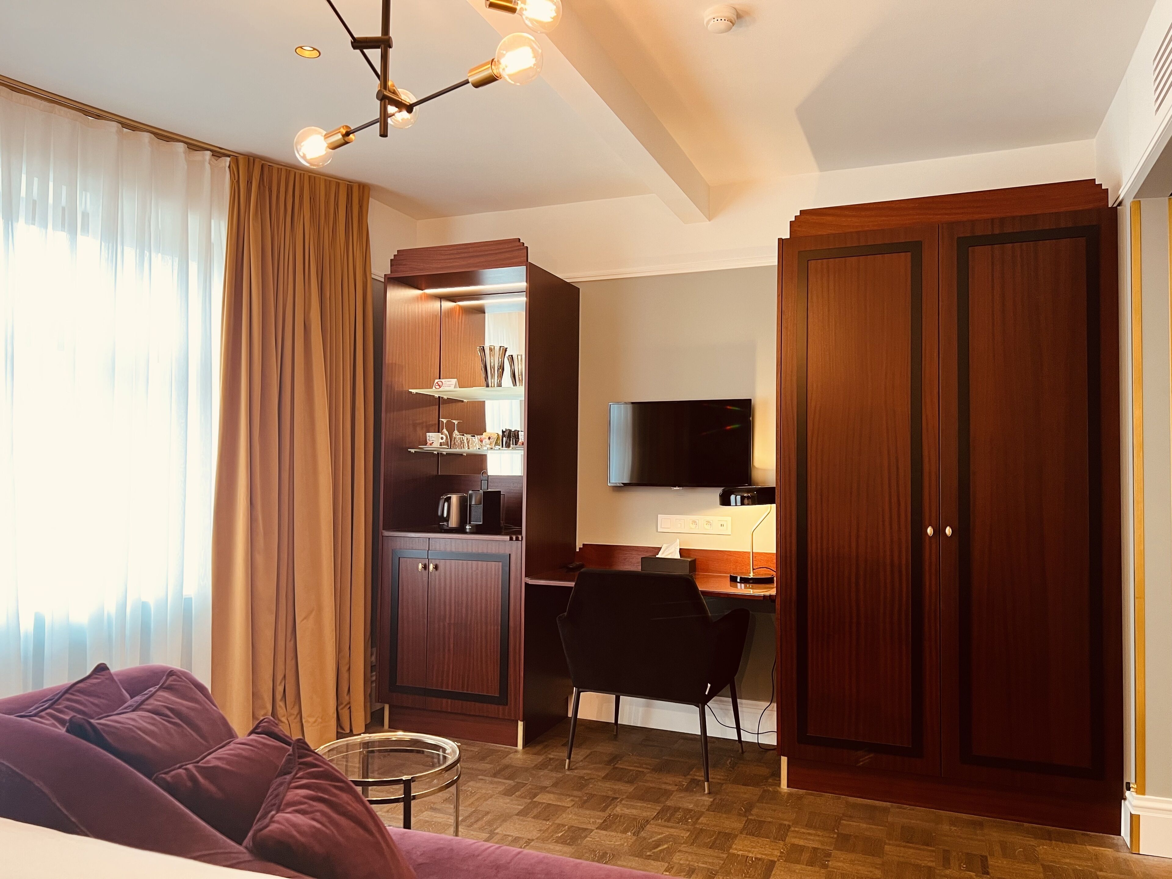 Ett modernt hotellrum med en soffa, ett skrivbord, en TV och en garderob.