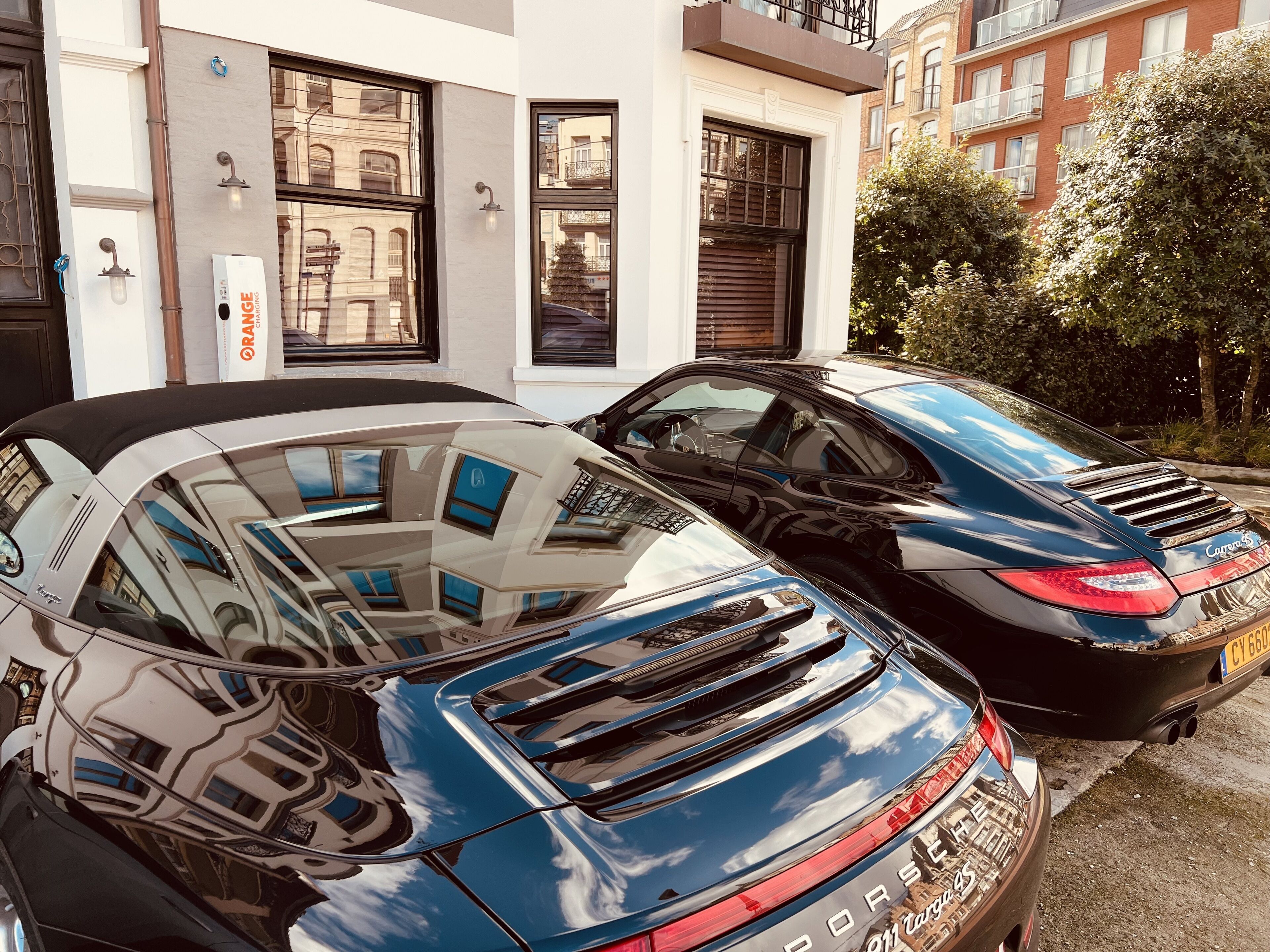 Zwei geparkte Autos vor einem Gebäude mit großen Fenstern und einer sichtbaren Tür.