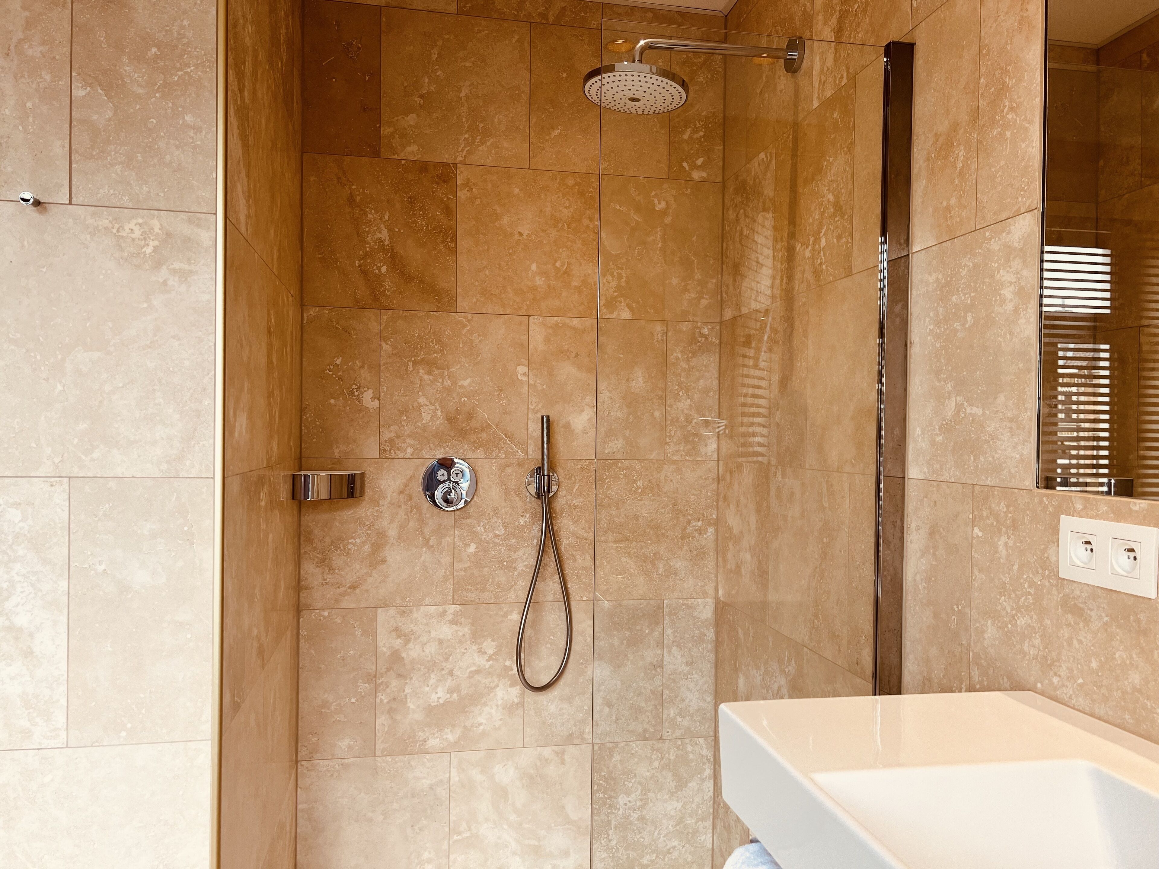 A modern bathroom with a walk-in shower, a handheld showerhead, and a wall-mounted faucet.