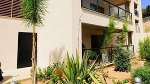 Un immeuble à plusieurs étages doté de balcons, entouré de jardins aménagés et surplombant un ciel dégagé.