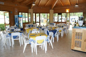 A restaurant with multiple tables and chairs, a refrigerator, and a wooden cabinet.