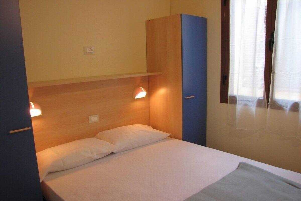 Una cama individual con cabecera de madera, un armario azul y una ventana con cortinas.