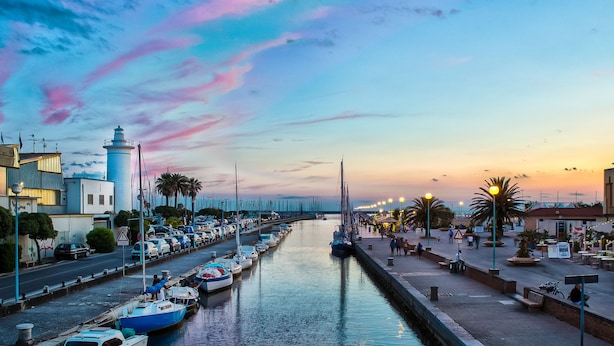 A marina with boats docked along a waterfront, a bridge in the background, and a sunset sky. - Camping Viareggio (Viareggio)