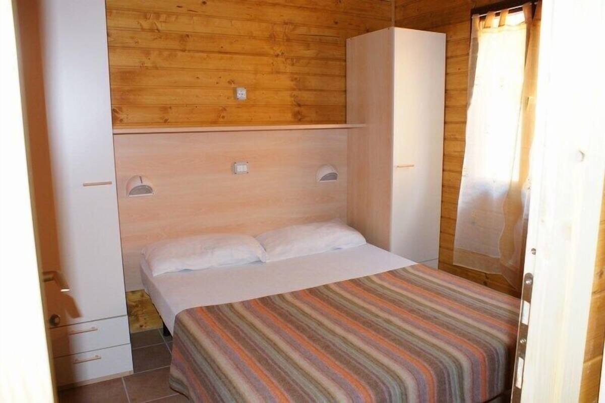 Una cama individual con una colcha a rayas en una habitación con paredes de madera y un armario blanco.