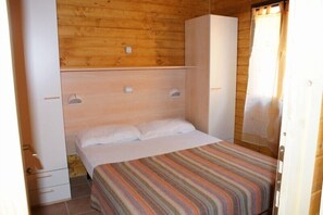 A single bed with a striped bedspread in a room with wooden walls and a white wardrobe.