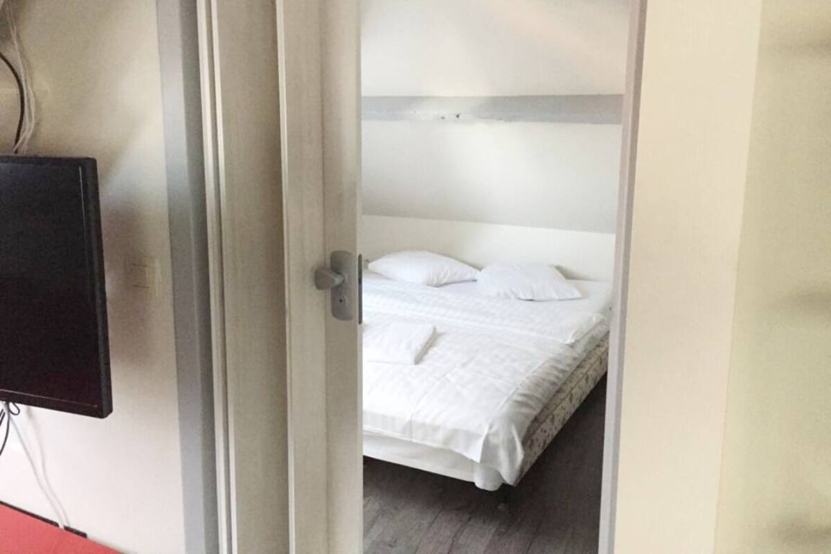 Una habitación con una cama, un televisor montado en la pared y una puerta que da a otra habitación.