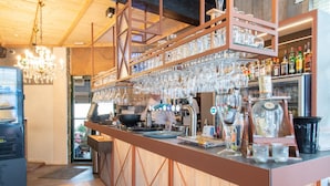 Een bar met een houten toonbank, planken met drinkglazen en diverse flessen.