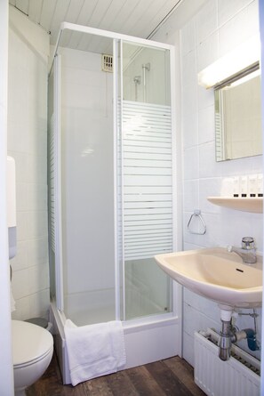 Een badkamer met een douchekabine van glas, een wit wastafeltje en een toilet.