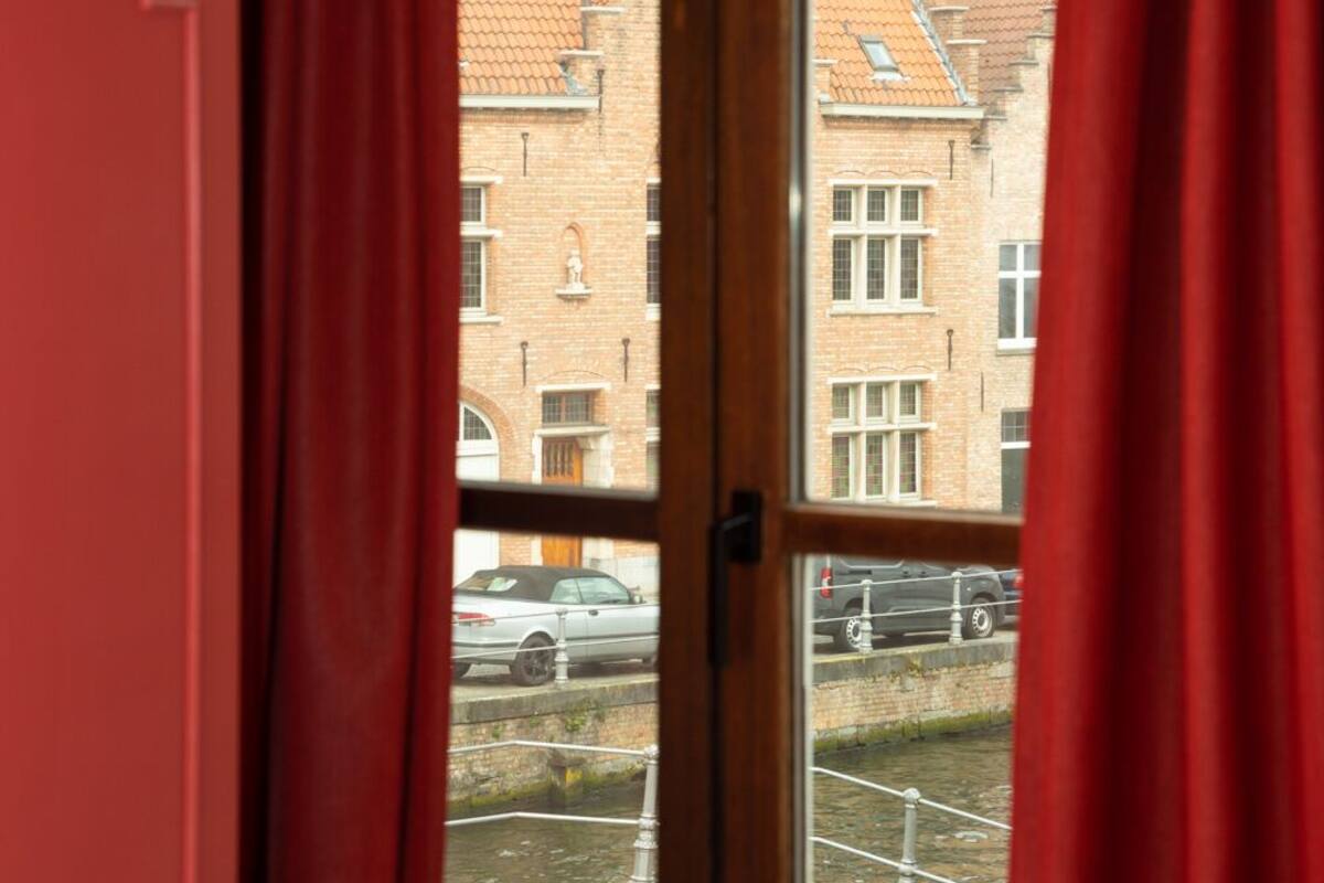 Una ventana con cortinas rojas, vista de un edificio de ladrillo y una persona montando en bicicleta afuera.