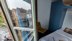 Een slaapkamer met een bed, een raam en uitzicht op gebouwen.