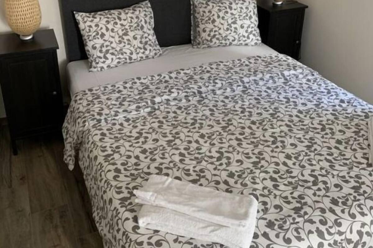 Una cama bien hecha con ropa de cama estampada, un espejo grande encima y dos lámparas de noche en mesitas oscuras.