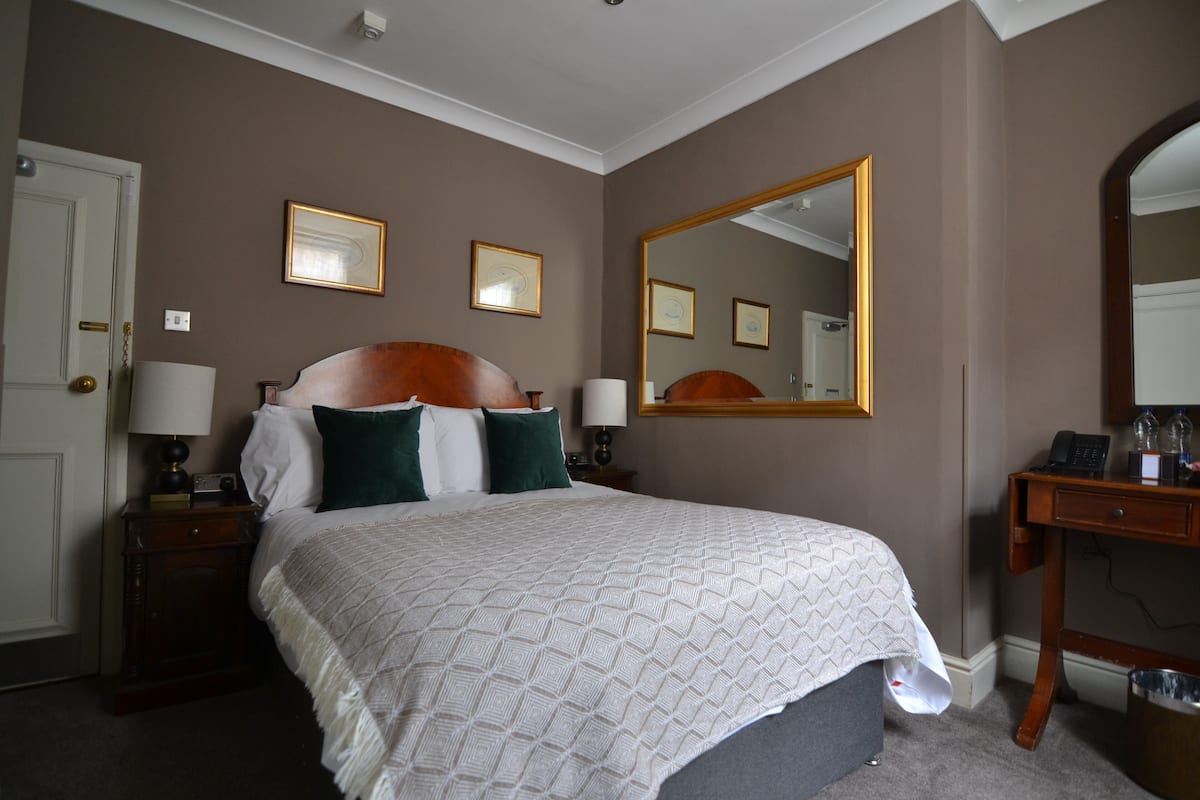A hotel room with a large bed, two bedside tables with lamps, a wooden dresser, and a large mirror on the wall.