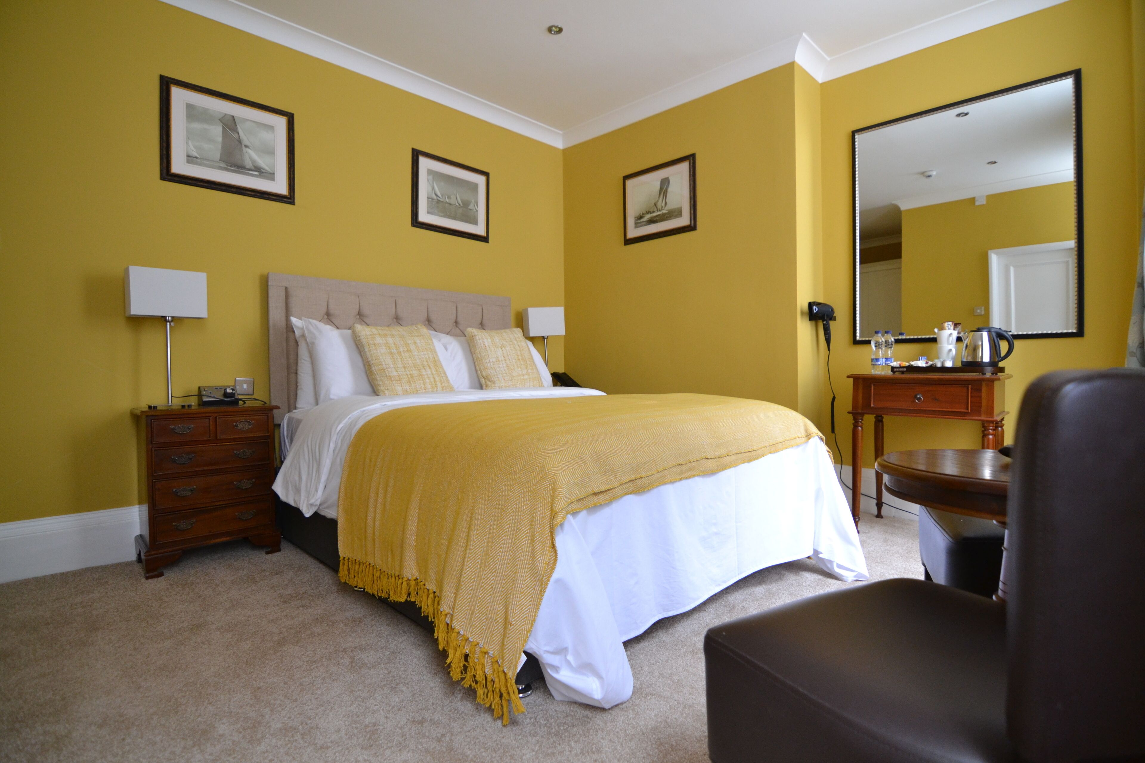 A hotel room with a bed, bedside tables, a chair, a dresser, a mirror, and framed pictures on the walls.
