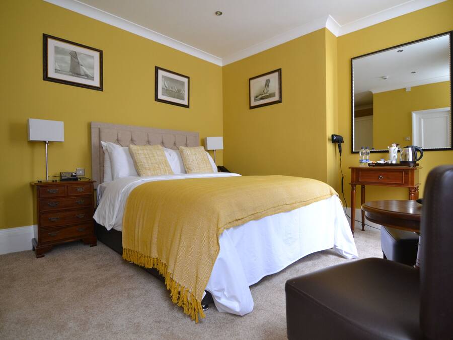 Ein Hotelzimmer mit Bett, Nachttischen, einem Sessel, einem Schminktisch und Spiegeln sowie gerahmten Bildern an den Wänden.
