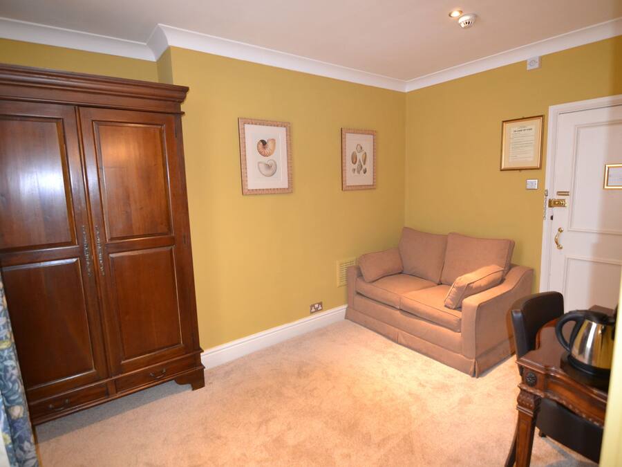 Una habitación con un armario grande de madera, un sofá color beige y una puerta con picaporte de latón.