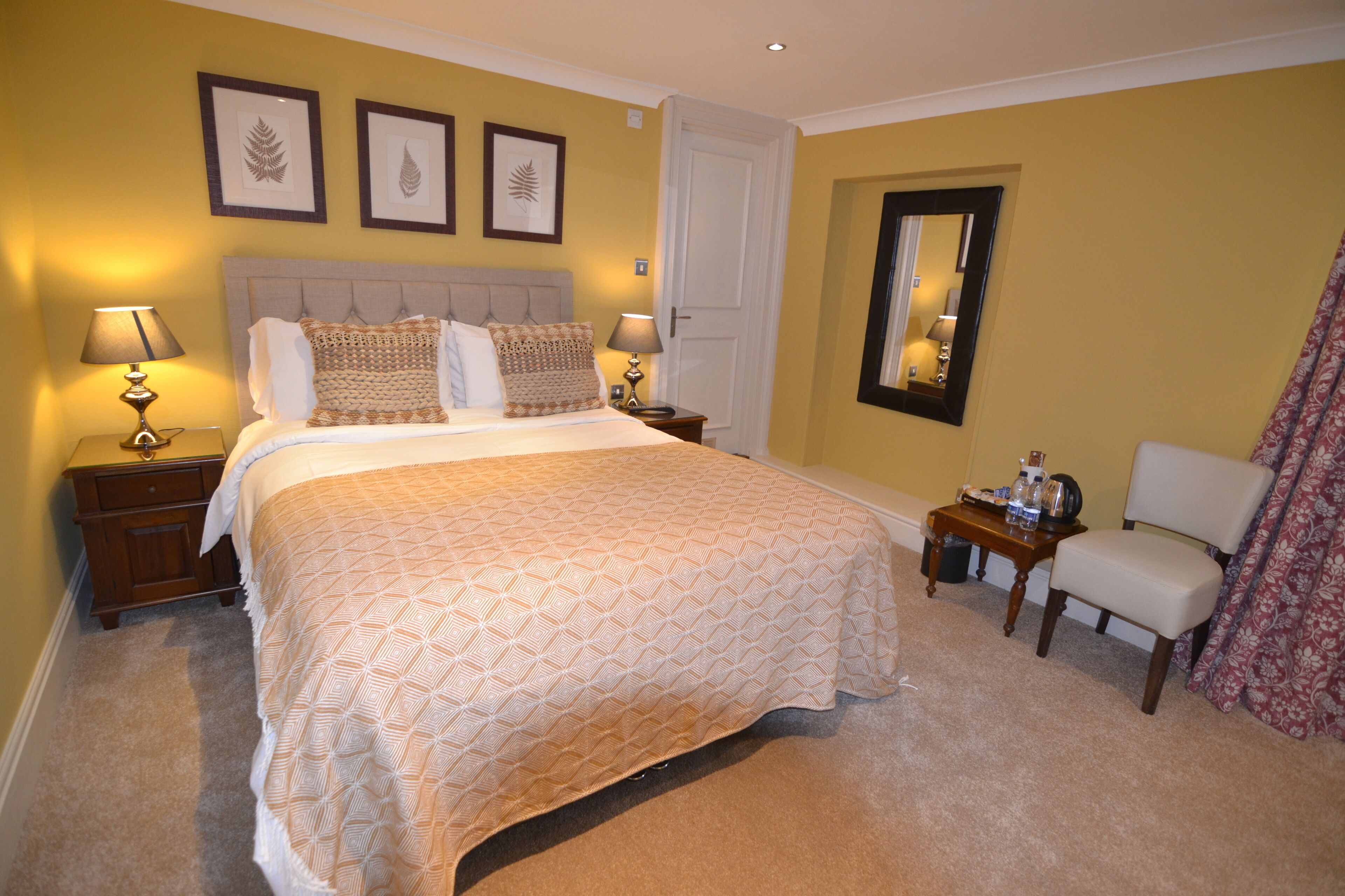 A neatly arranged bedroom with a large bed, two bedside tables with lamps, a chair, and a mirror on the wall.