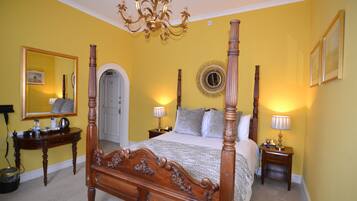 A four-poster bed with a mirror above it, bedside tables with lamps, and a chandelier.