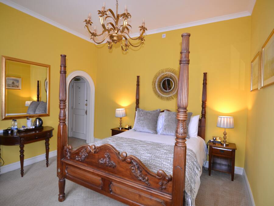 A four-poster bed with a mirror above it, bedside tables with lamps, and a chandelier.