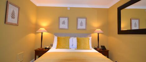 A hotel room with a bed, two bedside lamps, a nightstand with a phone, and framed leaf artwork on the walls.
