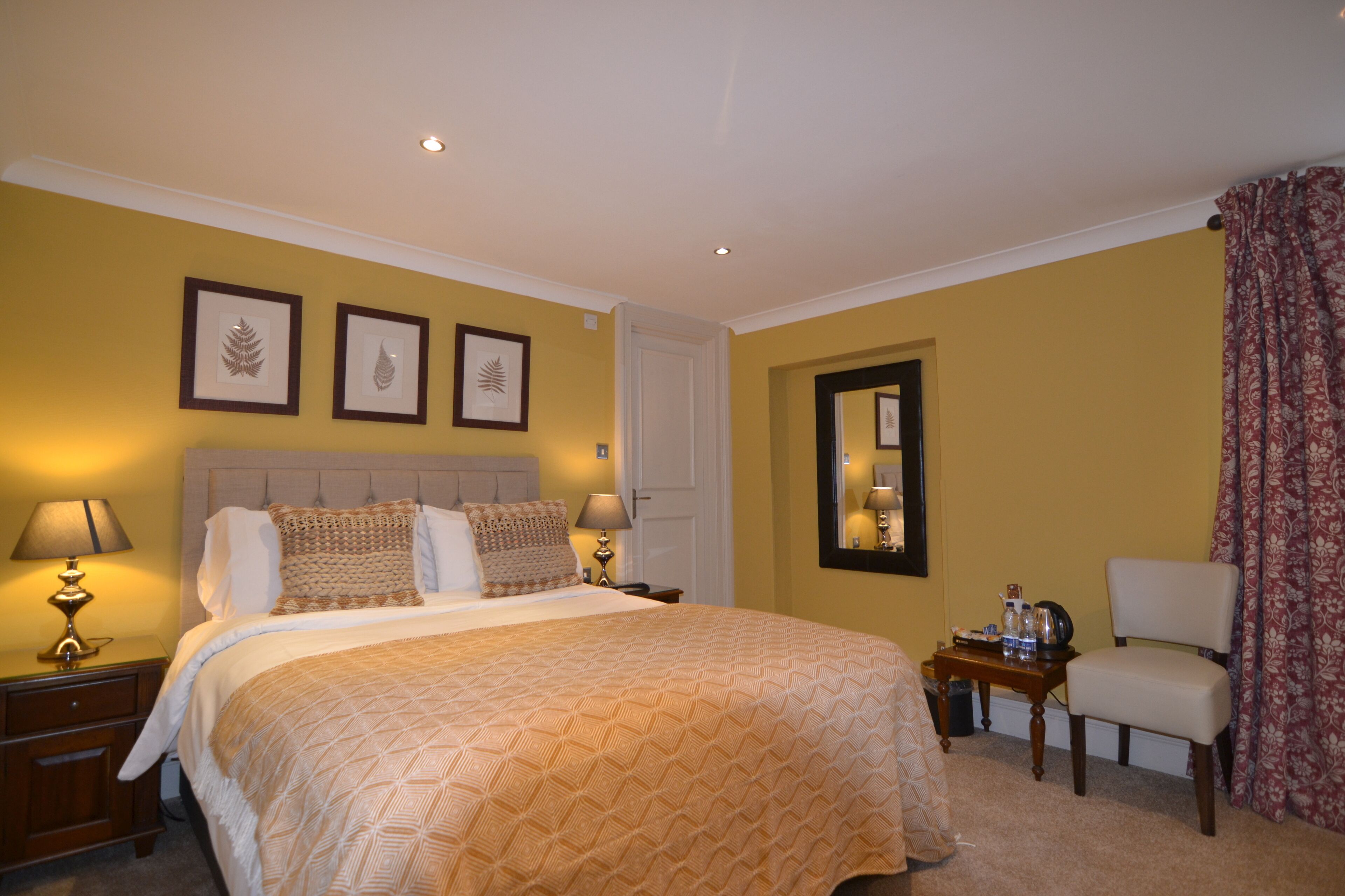 Habitación de hotel con una cama grande, dos mesitas de noche con lámparas, una silla y cuadros en la pared.