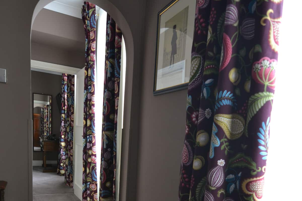 A hallway with patterned curtains, a framed picture on the wall, and a carpeted floor.