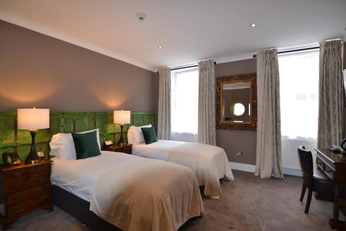 A hotel room with two beds, a desk, a chair, a mirror, and a window with curtains.