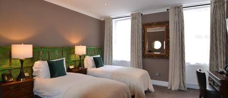A hotel room with two beds, a desk, a chair, a mirror, and a window with curtains.