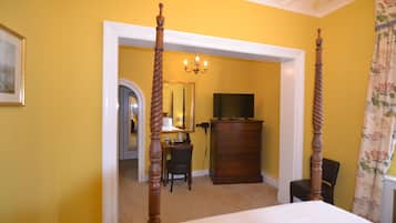 A bedroom with a four-poster bed, a dresser, a television, and a desk with a chair.