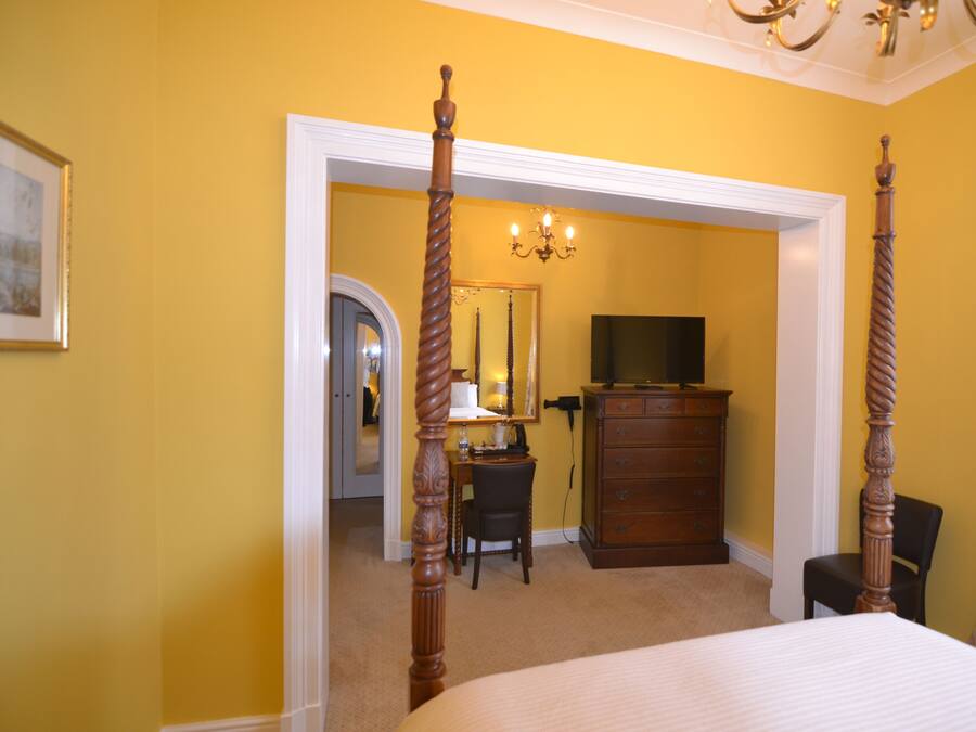 A bedroom with a four-poster bed, a dresser, a television, and a desk with a chair.
