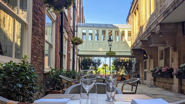An outdoor dining area with a table set for two, two wine glasses, and a menu. - Angel & Royal Hotel (Grantham)