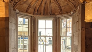 A room with a red velvet sofa, a wooden floor, and a large arched window with a view of the street. - Angel & Royal Hotel (Grantham)