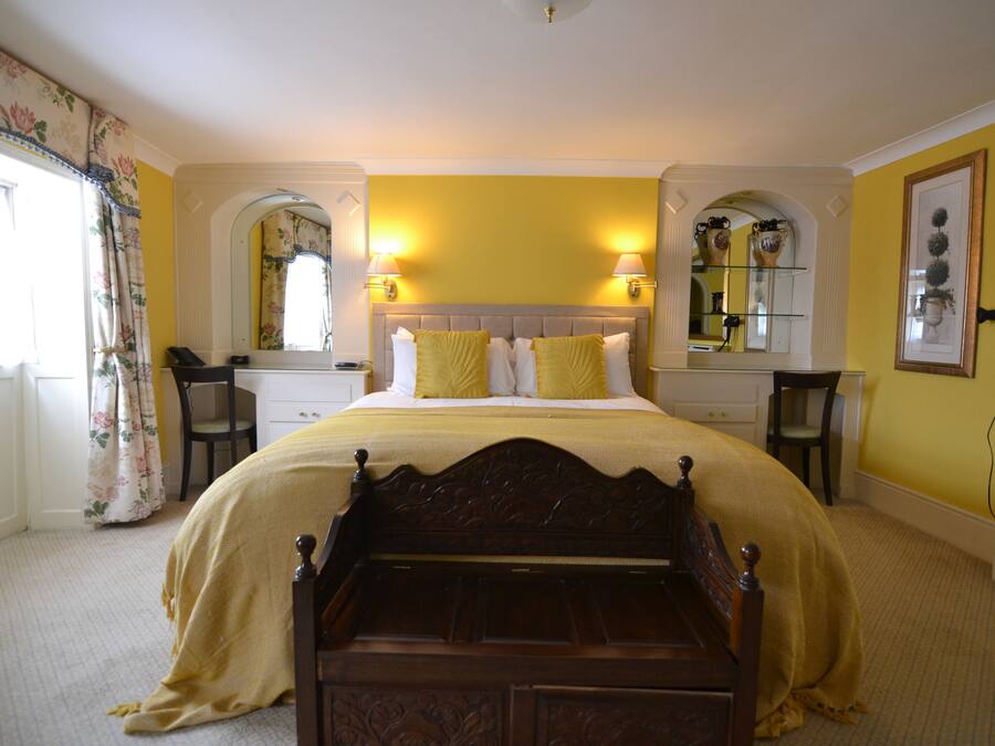 A bedroom with a large bed, two bedside tables, a nightstand, a mirror, and a window with curtains.