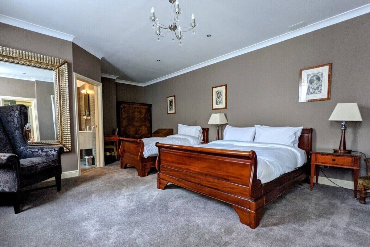 A bedroom with two wooden beds, a large mirror, a chandelier, and framed pictures on the wall.