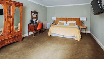 A bedroom with a bed, a wooden wardrobe, a desk with a chair, a television, and a radiator.