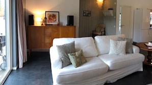 A modern living room with a white sofa, a wooden cabinet, and a wall-mounted light fixture.