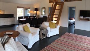 A spacious living area with a staircase leading to an upper level, a dining area, and a television mounted on the wall.