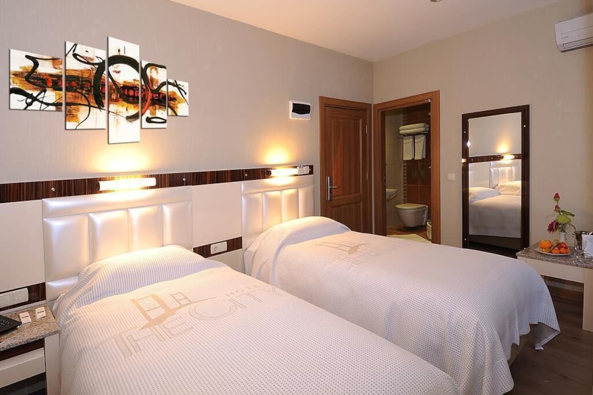A hotel room with two beds, a large mirror, a wall art piece, and a bathroom visible through an open door.