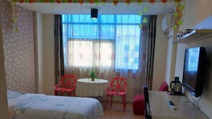 Una habitación de hotel con dos camas, un escritorio con televisor, una pequeña mesa con sillas y una ventana con cortinas.