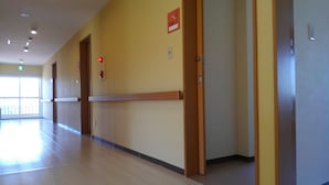 Un long couloir bien éclairé, avec un plancher et des portes en bois, un détecteur d’incendie et un panneau indiquant le numéro de la porte sur le mur.