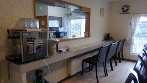 Une petite cuisine équipée d’une machine à café, d’un four à micro-ondes et d’un réfrigérateur. Des chaises sont à disposition, et une fenêtre offre une vue agréable.