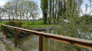 A wooden bridge over a calm river with trees and greenery in the background. - Roulotte à la Ferme de l'Isle (Avaray)