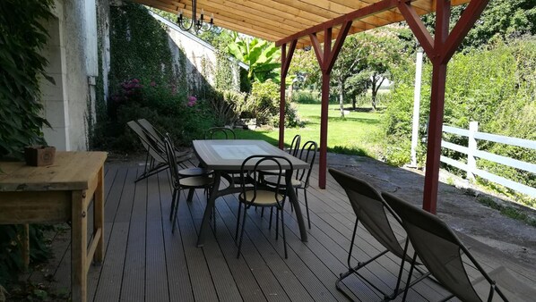 An outdoor patio with a wooden table and chairs, surrounded by a white fence and lush greenery.
