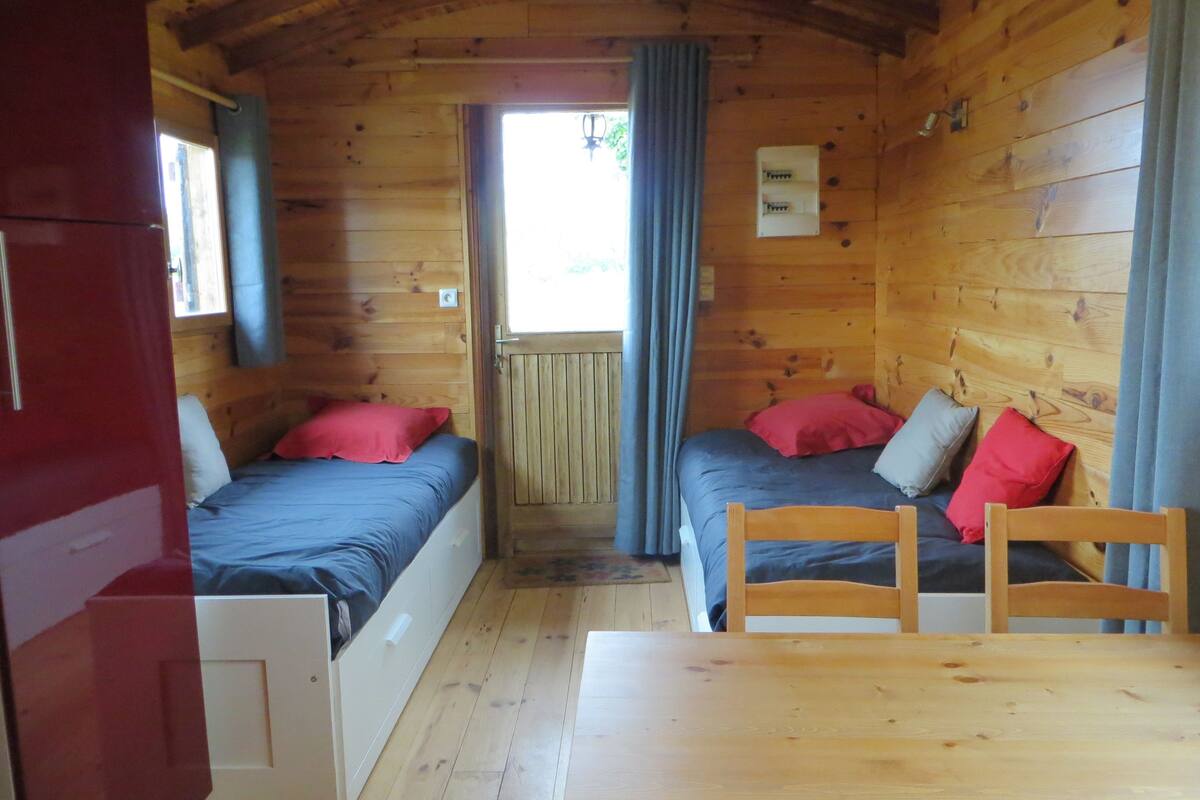 A cabin with two wooden beds, a wooden table, and a window with curtains.